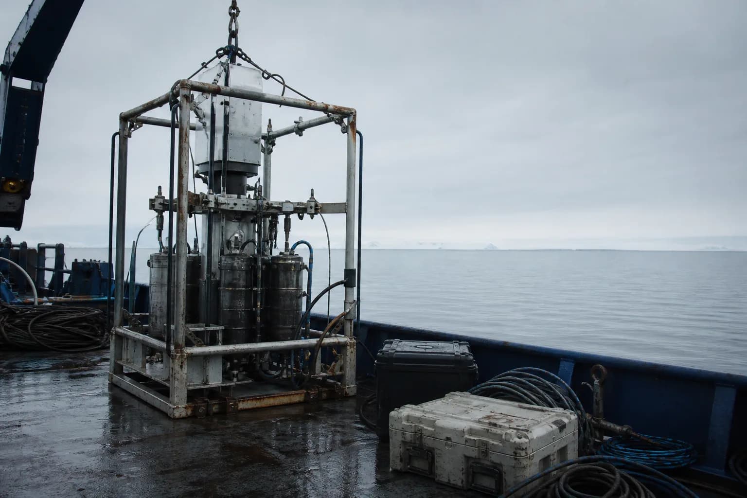 A steel seabed instrument frame on a research vessel deck, salt-stained, cables coiled beside it in low arctic light.
